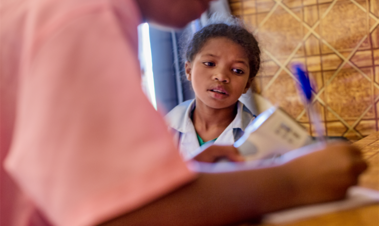 A female child sitting and looking as a nurse writes in notebook in rural clinic of nutrition enhancement program in Madagascar.