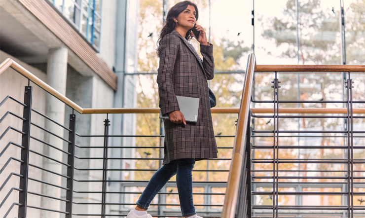 Vrouw met telefoon en Surface in een kantoorgebouw