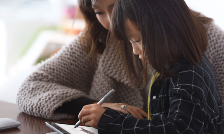 a woman and child sitting at a table using a laptop
