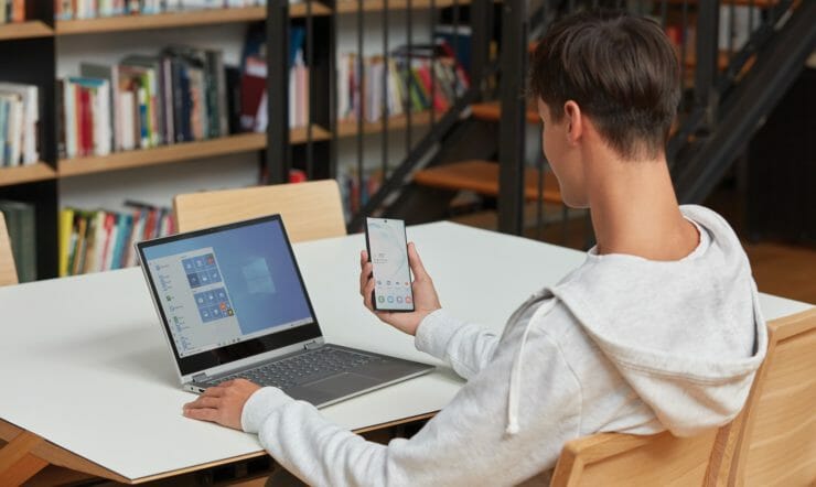 a man using a laptop computer sitting on top of a book shelf
