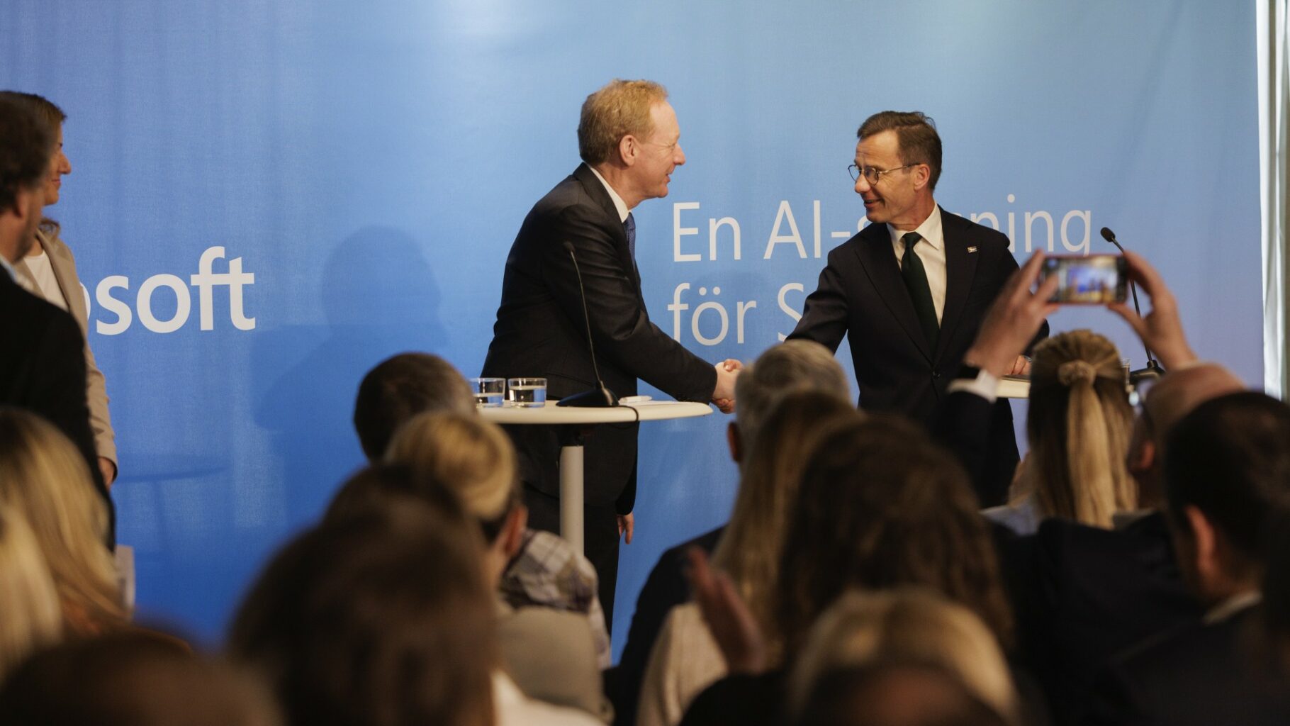 Två personer skakar hand på en scen framför en publik.
